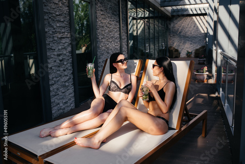 Two sexy girlfriends drink coctails at the pool