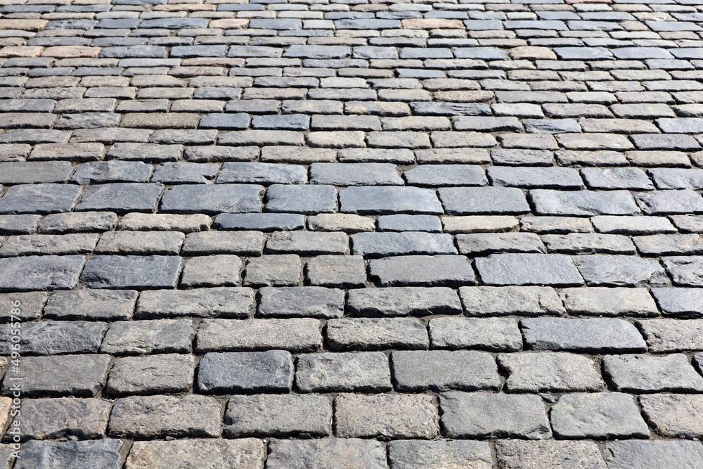 Stone pavement texture, cobbled street in sunlight. Old paved road with tiles from cobblestones