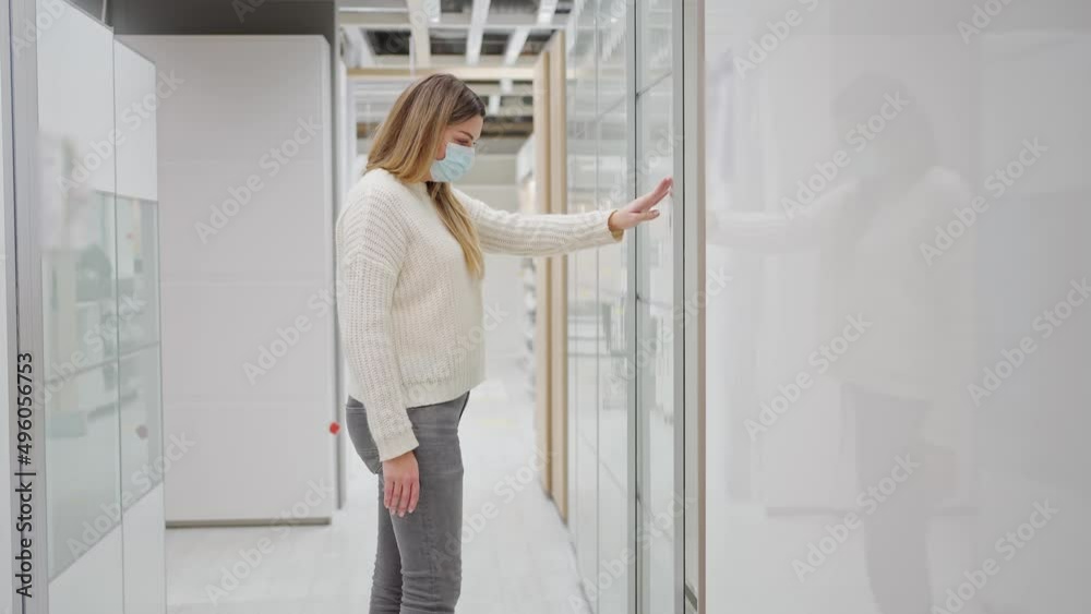 a young woman in a protective mask chooses a wardrobe in a store. moves tall cabinet doors to the side a young woman in a protective mask chooses a wardrobe in a store. moves tall cabinet doors to the side