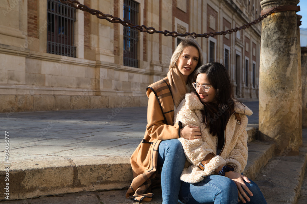 lesbian couple sitting on the steps of a pavement in a monumental square in old europe. They are very much in love and happy. Concept tourism and travel, lgtb. Rights and equality.