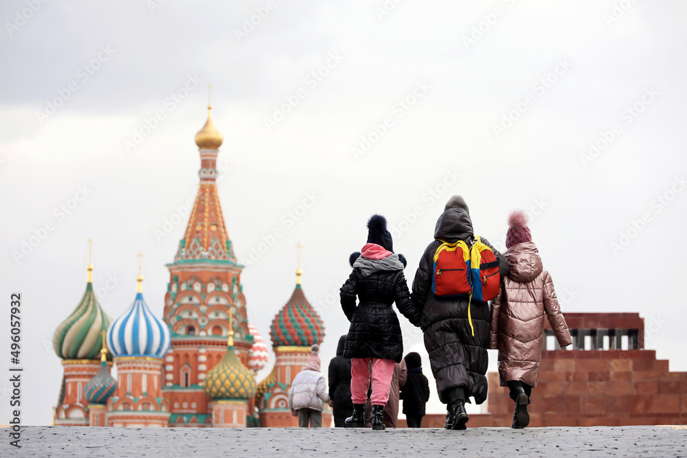 People walking on Red square in Moscow on background of St. Basil's Cathedral and Lenin Mausoleum. Woman with two kid girls in the foreground, spring weather in Russia
