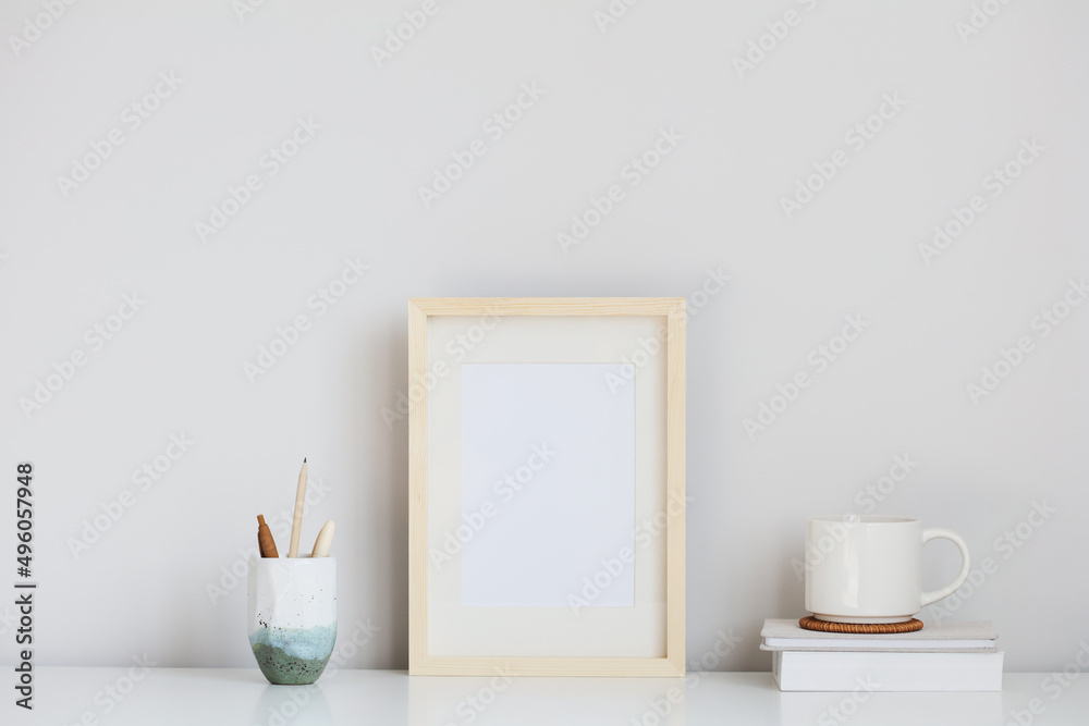 Picture frame mockup, office stationery, cup of coffee, books on white table. Elegant modern workspace, nordic style.