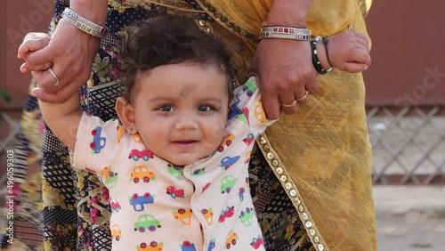 A small Indian smiles at the child holding both the hands as the mother stands up (first steps of baby )