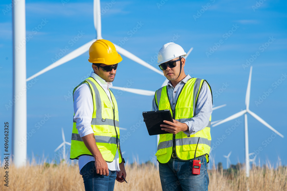 Engineer wearing uniform ,helmet hold document inspection work in wind turbine farms rotation to generate electricity energy. Green ecological power energy generation wind sustainable energy concept. Engineer wearing uniform ,helmet hold document inspection work in wind turbine farms rotation to generate electricity energy. Green ecological power energy generation wind sustainable energy concept.