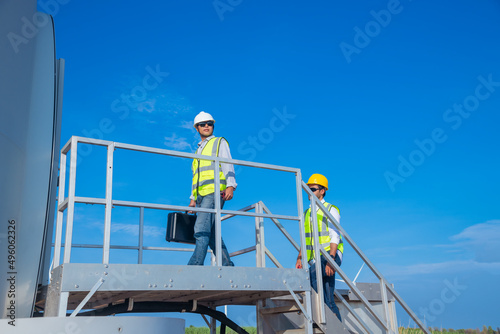 Engineer wearing uniform ,helmet hold document inspection work in wind turbine farms rotation to generate electricity energy. Green ecological power energy generation wind sustainable energy concept. © APchanel