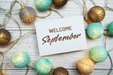 Welcome September text on paper card with LED cotton balls top view on wooden background