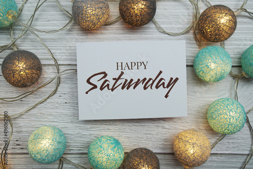 Happy Saturday text on paper card with LED cotton balls top view on wooden background