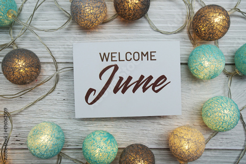Welcome June text on paper card with LED cotton balls top view on wooden background