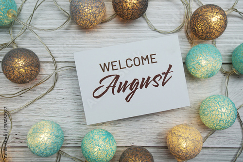 Welcome August text on paper card with LED cotton balls top view on wooden background