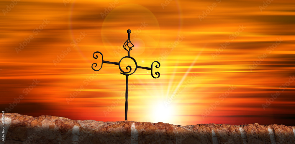Fototapeta premium Close-up of a wrought iron religious cross above a red marble altar, against a beautiful sunset sky with sunbeams and copy space.
