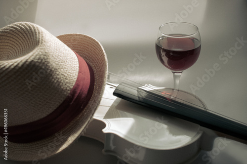 Romantic plot with a white violin and a glass of red wine on a gray background, with a straw hat with a red piping