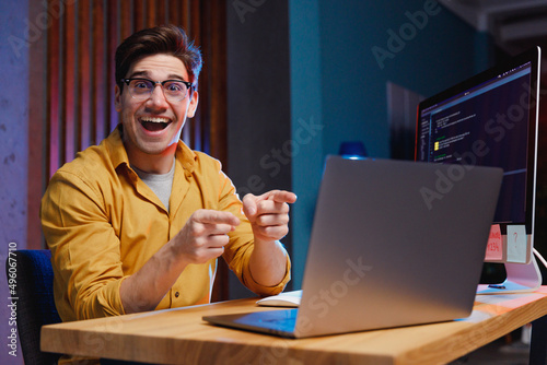 Foto Young surprised happy winner amazed successful software engineer IT specialist programmer man in shirt work at home office writing code point finger on laptop pc computer