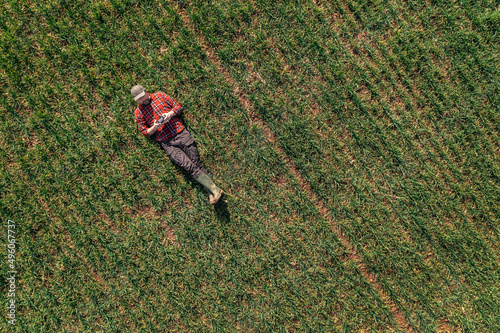 Farmer laying on the ground and using drone remote controller to observe cultivated wheat field photo