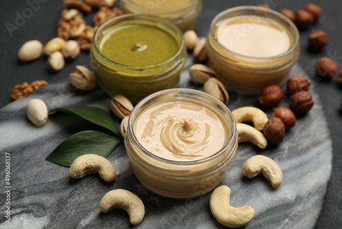 Jars with butters made of different nuts and ingredients on black table, closeup