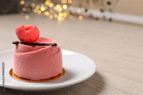 Delicious mousse cake with floral decor on white wooden table against blurred lights, closeup. Space for text