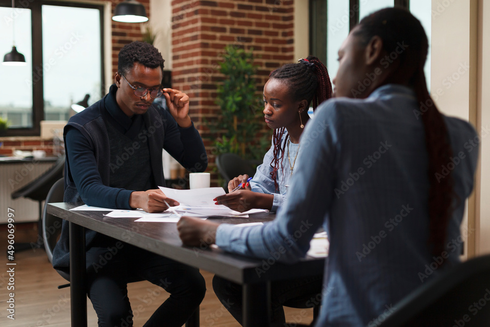 African american research agency coworkers in meeting about startup project financial status. Business people at desk in company office finance department talking about marketing expenses.