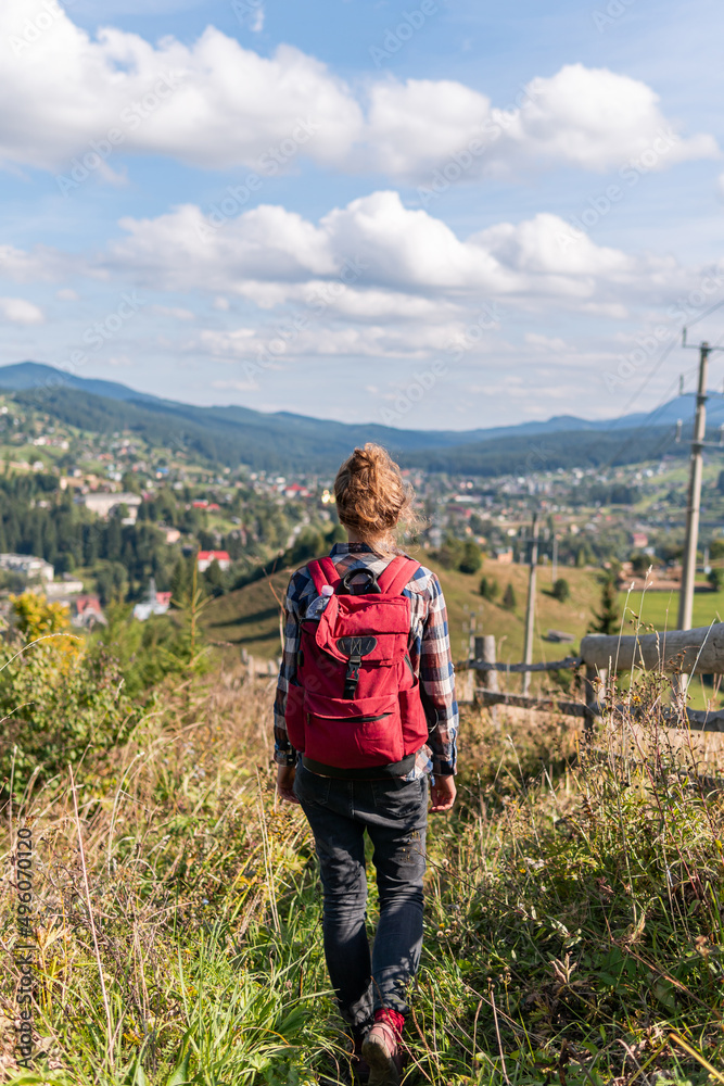 A young woman, tourist is walking is walking in the mountains with backpack on a warm summer day