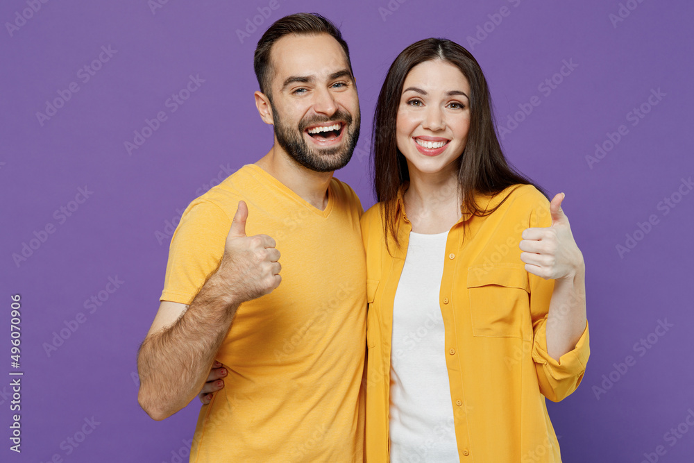 Fototapeta premium Young cheerful happy fun couple two friends family man woman together in yellow casual clothes looking camera showing thumb up like gesture cuddle isolated on plain violet background studio portrait.