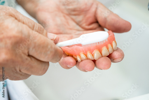 Asian senior or elderly old woman patient use toothbrush to clean partial denture of replacement teeth. photo