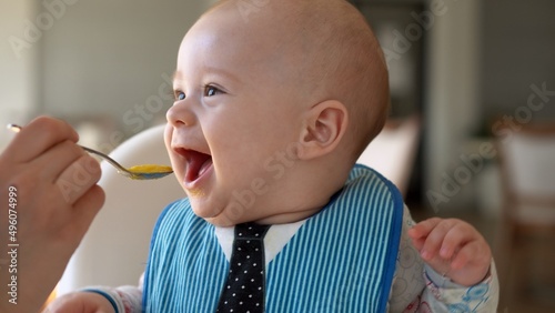 Childhood, Happiness, family, Motherhood. Cheerful happy smiling baby Close up face. Emotions of newborn boy. child in a bib sits in a feeding chair gnaws toothpick in the kitchen, Infant gum pain