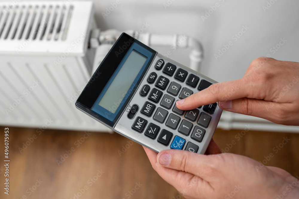 heating, energy crisis and consumption concept - close up of hand with calculator and radiator at home heating, energy crisis and consumption concept - close up of hand with calculator and radiator at home