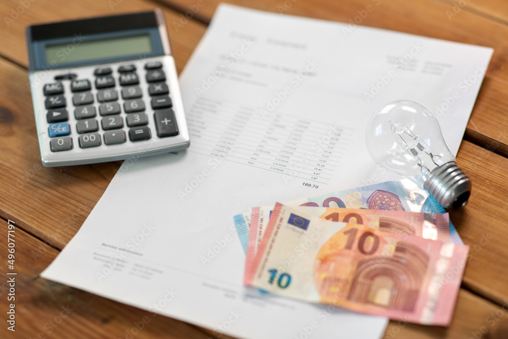 electricity, energy crisis and power consumption concept - close up of utility bill, calculator, money and lightbulb on wooden table electricity, energy crisis and power consumption concept - close up of utility bill, calculator, money and lightbulb on wooden table