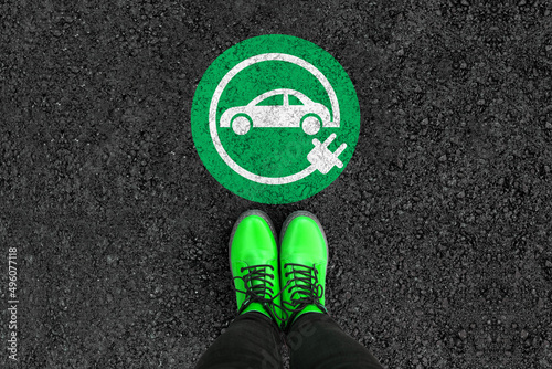 a woman with a boots is standing next to electric car sign on road asphalt 