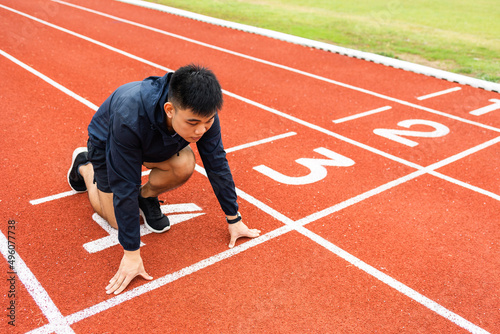 Young handsome chinese man doing star pose before running exercise on track in sport stadium. Challenge race of athletes running in the starting point