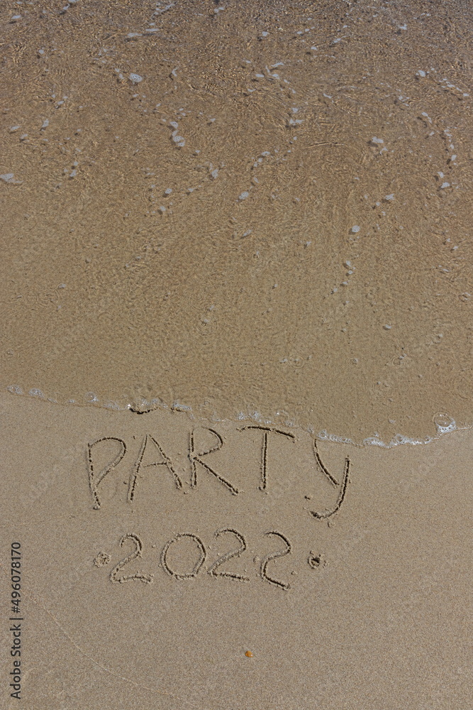 Fototapeta premium The inscription beach party 2022 on the sand by the water and the rising wave, seashore beach vacation by the sea