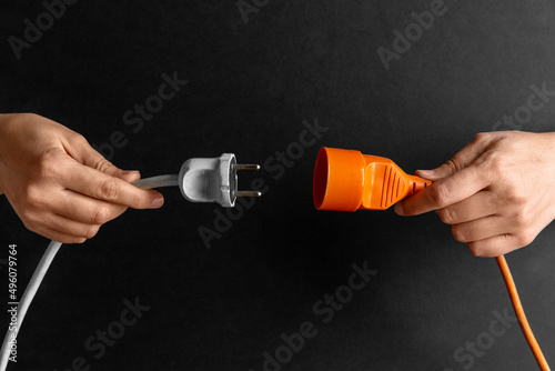 electricity, energy and power consumption concept - close up of woman inserting plug into socket over black background