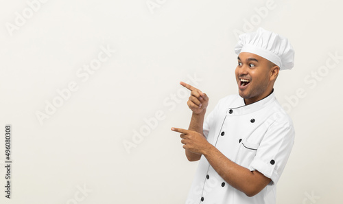 Smiling Young handsome asian man chef in uniform with hat standing pointing finger on isolated blank space for text. Cooking man Occupation chef or baker People in kitchen restaurant and hotel.