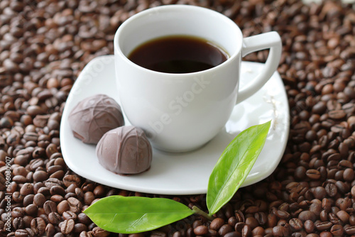 White cup of coffee with chocolate candy close up on coffee beand background