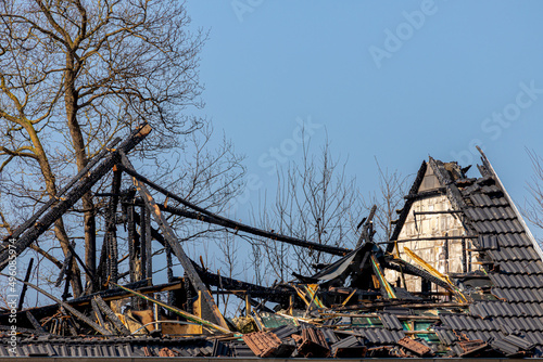 Conflagration concept, Damaged and broken roof top of the house, Destroyed house from fire with blue sky and trees as background, Burned wooden roof and bricks tile.