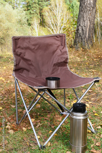 Folding tourist chair and thermos against backdrop of autumn forest