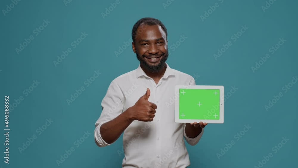 Happy man pointing at digital tablet with horizontal green screen in hand, showng isolated copy space with blank chroma key template and mockup background. Modern display technology. Happy man pointing at digital tablet with horizontal green screen in hand, showng isolated copy space with blank chroma key template and mockup background. Modern display technology.