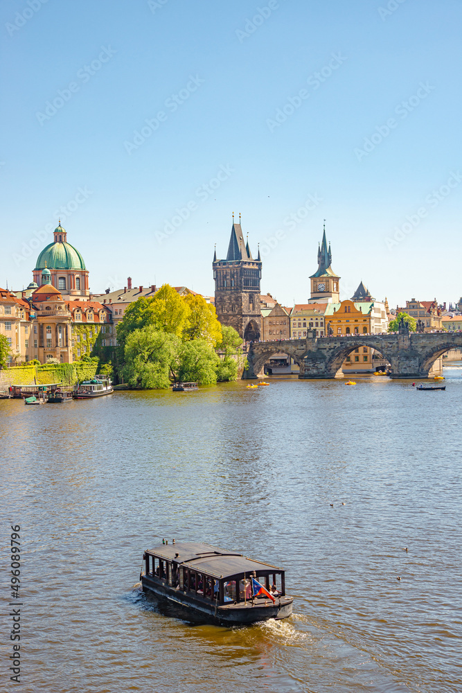 Naklejka premium View over magnificent Vltava river with tour boats, tourists and famous Charles Bridge and walking embarkment in historical downtown of Prague, Czech Republic at blue sunset summer sky.