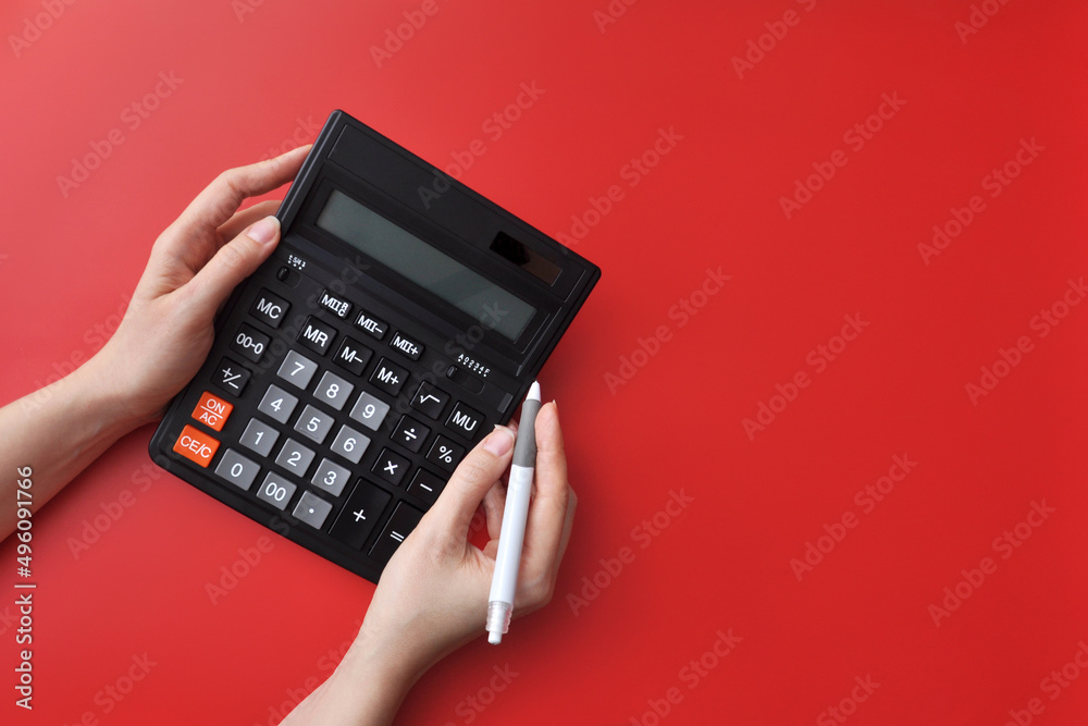 A black calculator in his hands on a red background. Symbol of data counting and problem solving A black calculator in his hands on a red background. Symbol of data counting and problem solving