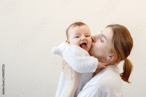portrait of a mother kissing a little smiling baby on a beige background