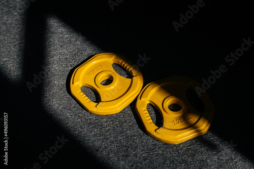 Yellow metal weight discs on a gray mat on a sunny day. Top view from above