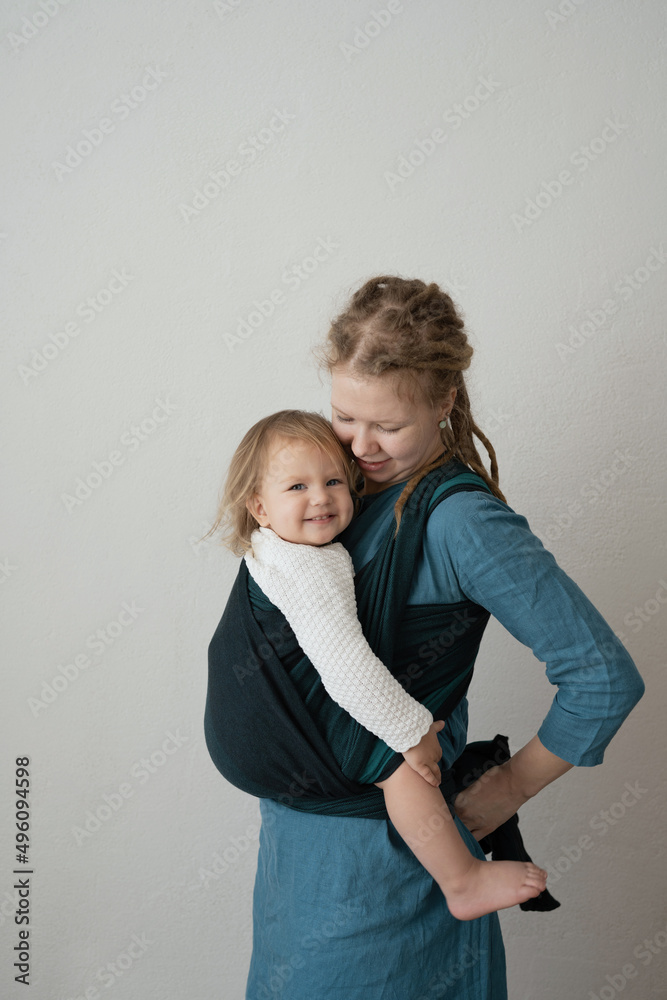 Mom in a sling with a happy daughter for the convenience of motherhood and taking care of the child. The modern mother chooses comfort. Mom in a sling with a happy daughter for the convenience of motherhood and taking care of the child. The modern mother chooses comfort.