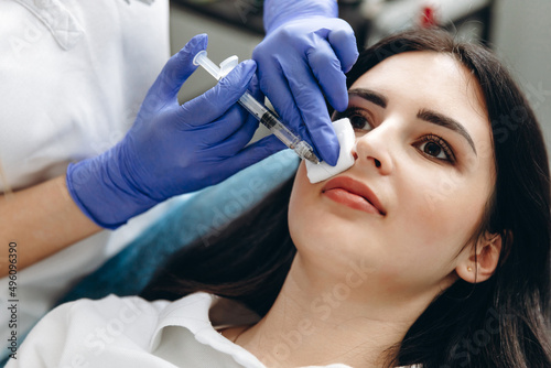 Attractive female doctor making an injection in patient's face wearing gloves photo