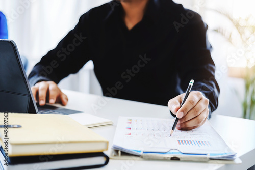 An accountant, businessman, auditor, economist man holding a pen pointing to a budget document and using tablet to examine and assess financial and investment risks for a company.