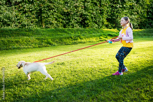 Young girl holds leash while walking puppy through park.