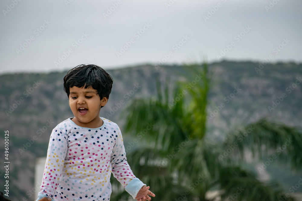 Small girl kid posing inside the forest with the backdrop of mountains went on a forest safari with her parents. Cute girl making different expressions while playing in outdoors. Small girl kid posing inside the forest with the backdrop of mountains went on a forest safari with her parents. Cute girl making different expressions while playing in outdoors.