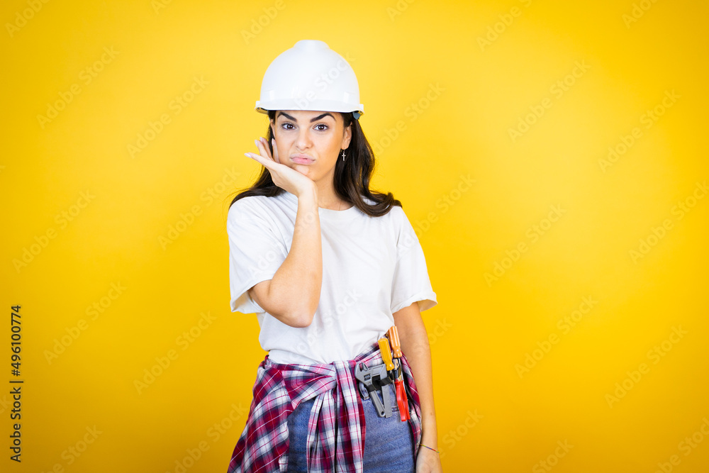 Young caucasian woman wearing hardhat and builder clothes over isolated yellow background thinking looking tired and bored with crossed arms