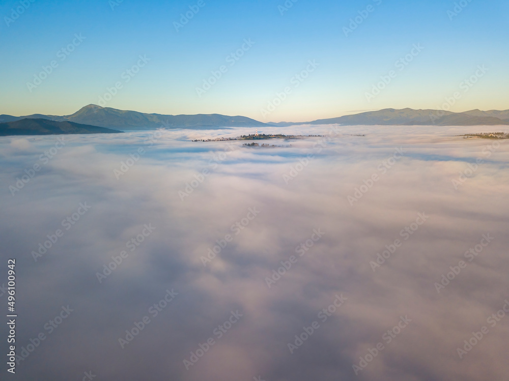 Flight over fog in Ukrainian Carpathians in summer. Mountains on the horizon. A thick layer of fog covers the mountains with a continuous carpet. Aerial drone view.