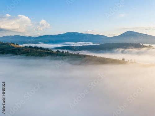 Flight over fog in Ukrainian Carpathians in summer. Mountains on the horizon. A thick layer of fog covers the mountains with a continuous carpet. Aerial drone view.