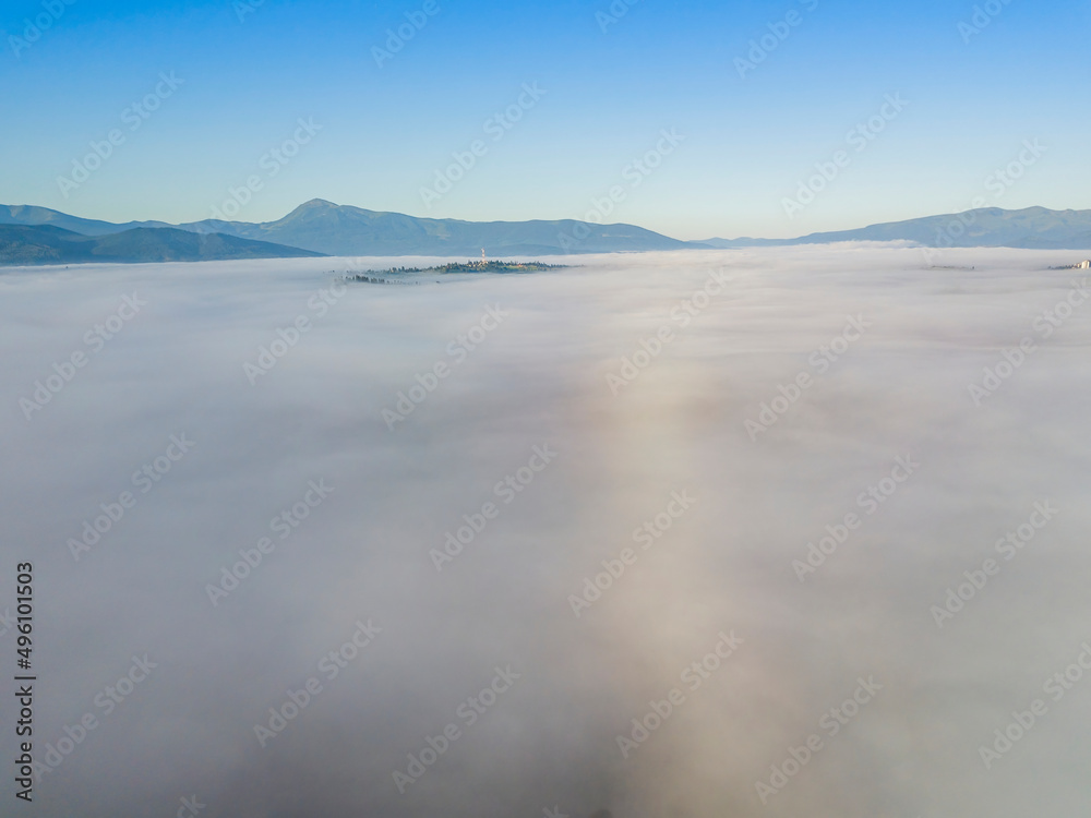 Flight over fog in Ukrainian Carpathians in summer. Mountains on the horizon. A thick layer of fog covers the mountains with a continuous carpet. Aerial drone view.