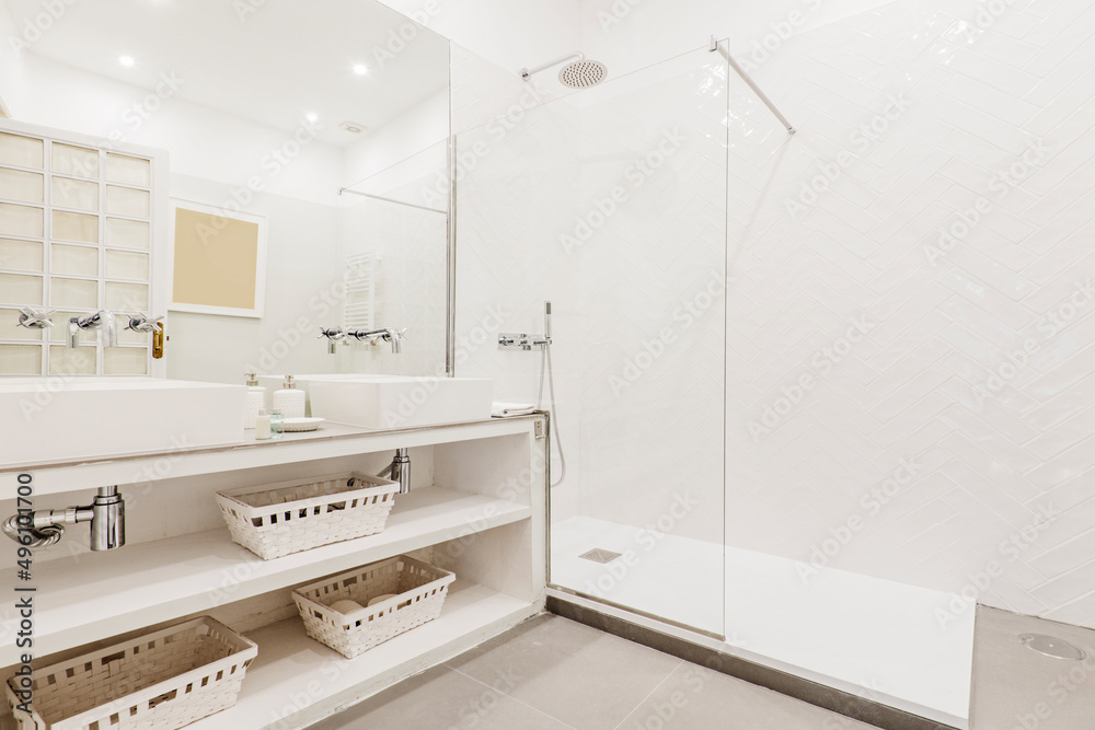 Bathroom with built-in vanity unit with white porcelain sink, wicker baskets, frameless mirror and glass-enclosed shower stall with vintage chrome taps Bathroom with built-in vanity unit with white porcelain sink, wicker baskets, frameless mirror and glass-enclosed shower stall with vintage chrome taps