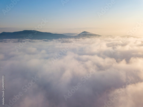 Flight over fog in Ukrainian Carpathians in summer. Mountains on the horizon. Aerial drone view.